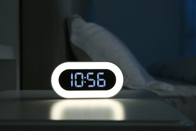 Photo of Digital alarm clock on bedside table in bedroom at night