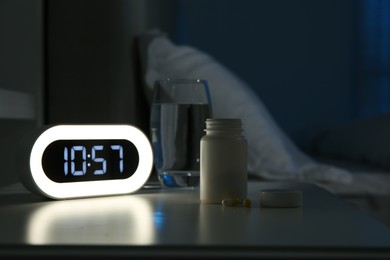 Insomnia treatment. Alarm clock, glass of water and pills on bedside table in bedroom at night