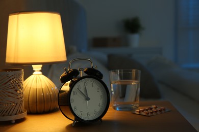 Insomnia treatment. Alarm clock, glass of water and pills on bedside table in bedroom at night