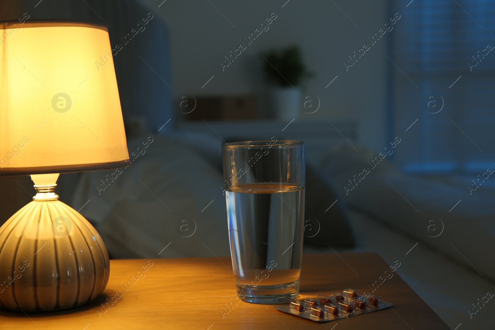 Photo of Insomnia treatment. Glass of water and pills on bedside table in bedroom at night