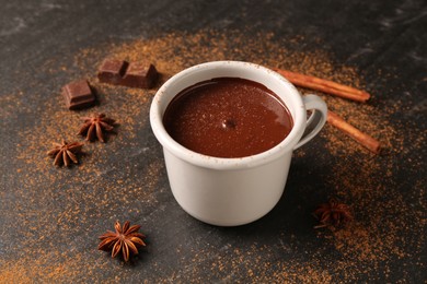 Photo of Tasty melted chocolate in cup and spices on dark textured table, closeup