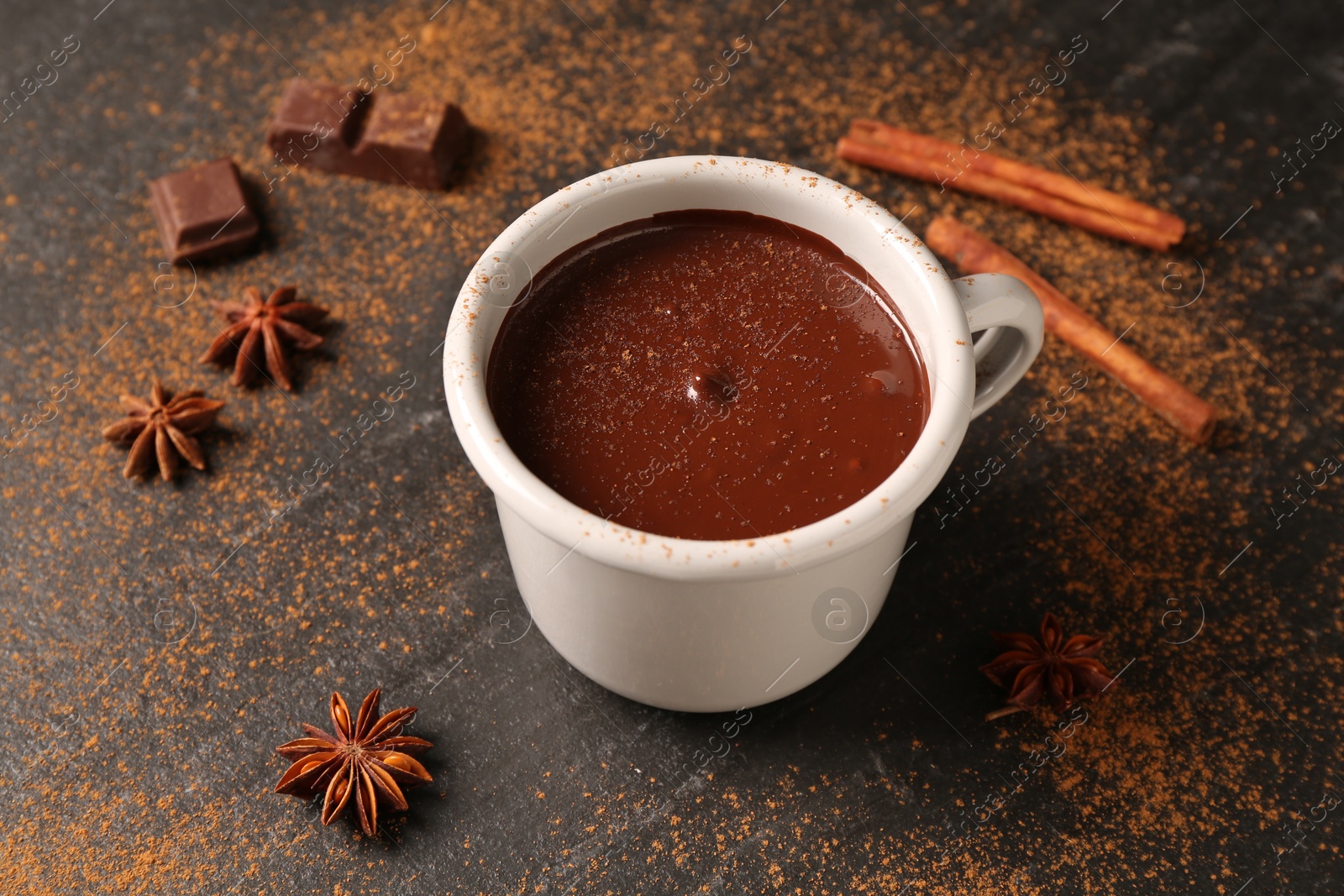 Photo of Tasty melted chocolate in cup and spices on dark textured table, closeup