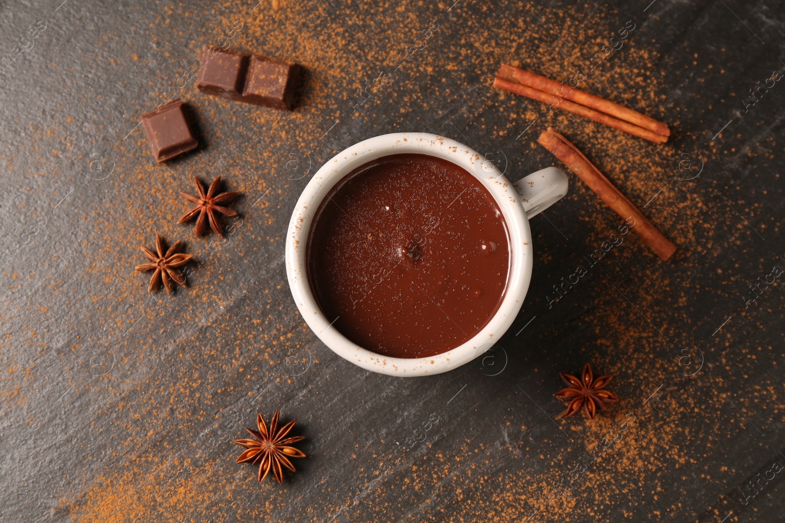 Photo of Tasty melted chocolate in cup and spices on dark textured table, flat lay