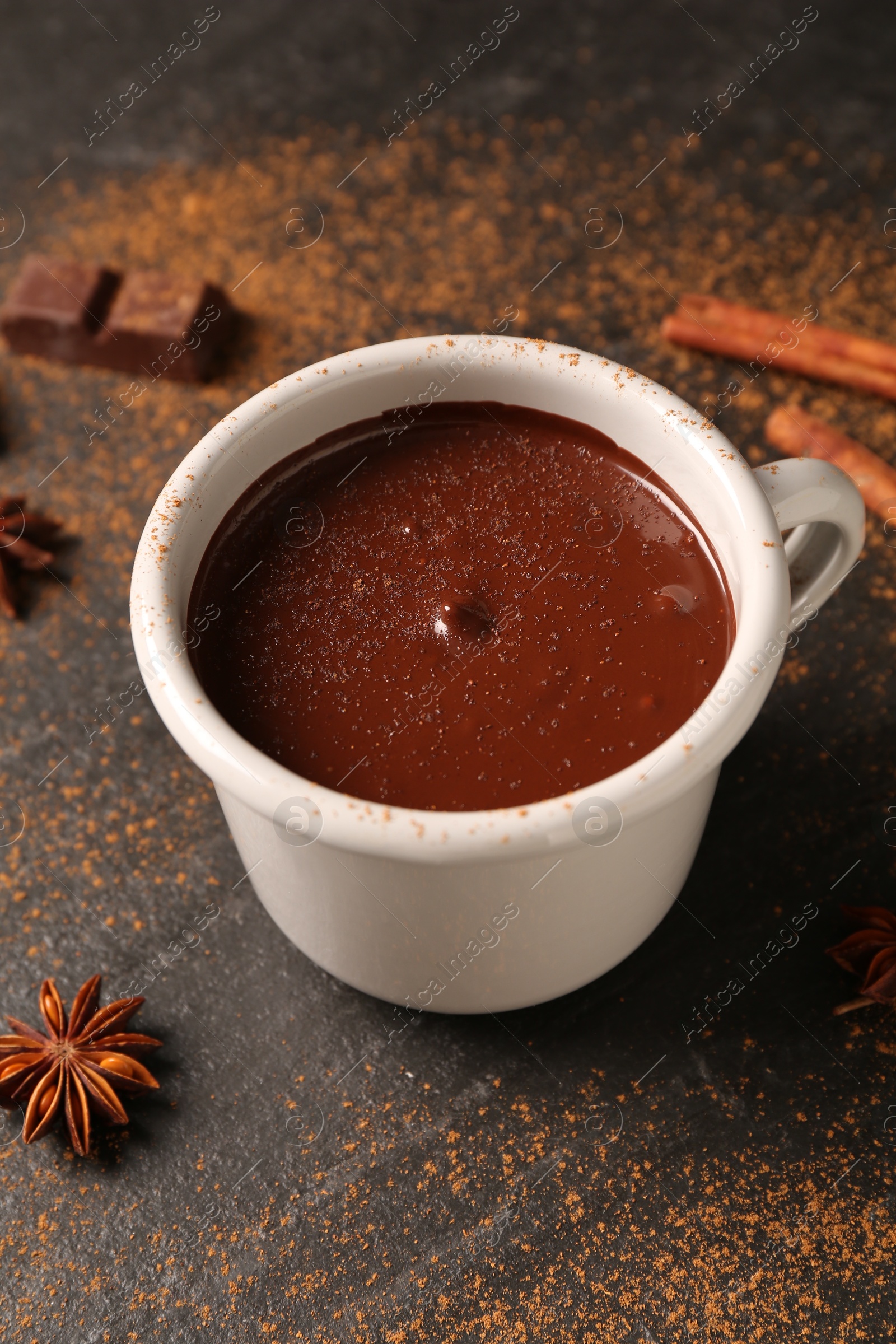 Photo of Tasty melted chocolate in cup and spices on dark textured table, closeup