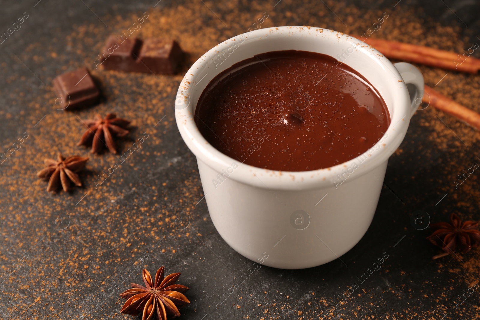 Photo of Tasty melted chocolate in cup and spices on dark textured table, closeup