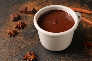 Tasty melted chocolate in cup and spices on dark textured table, closeup