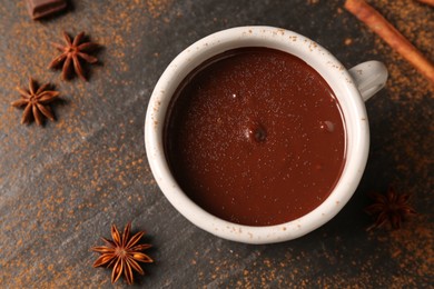 Photo of Tasty melted chocolate in cup and spices on dark textured table, flat lay