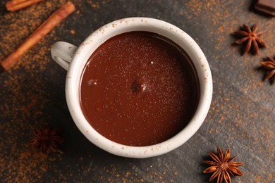 Photo of Tasty melted chocolate in cup and spices on dark textured table, flat lay