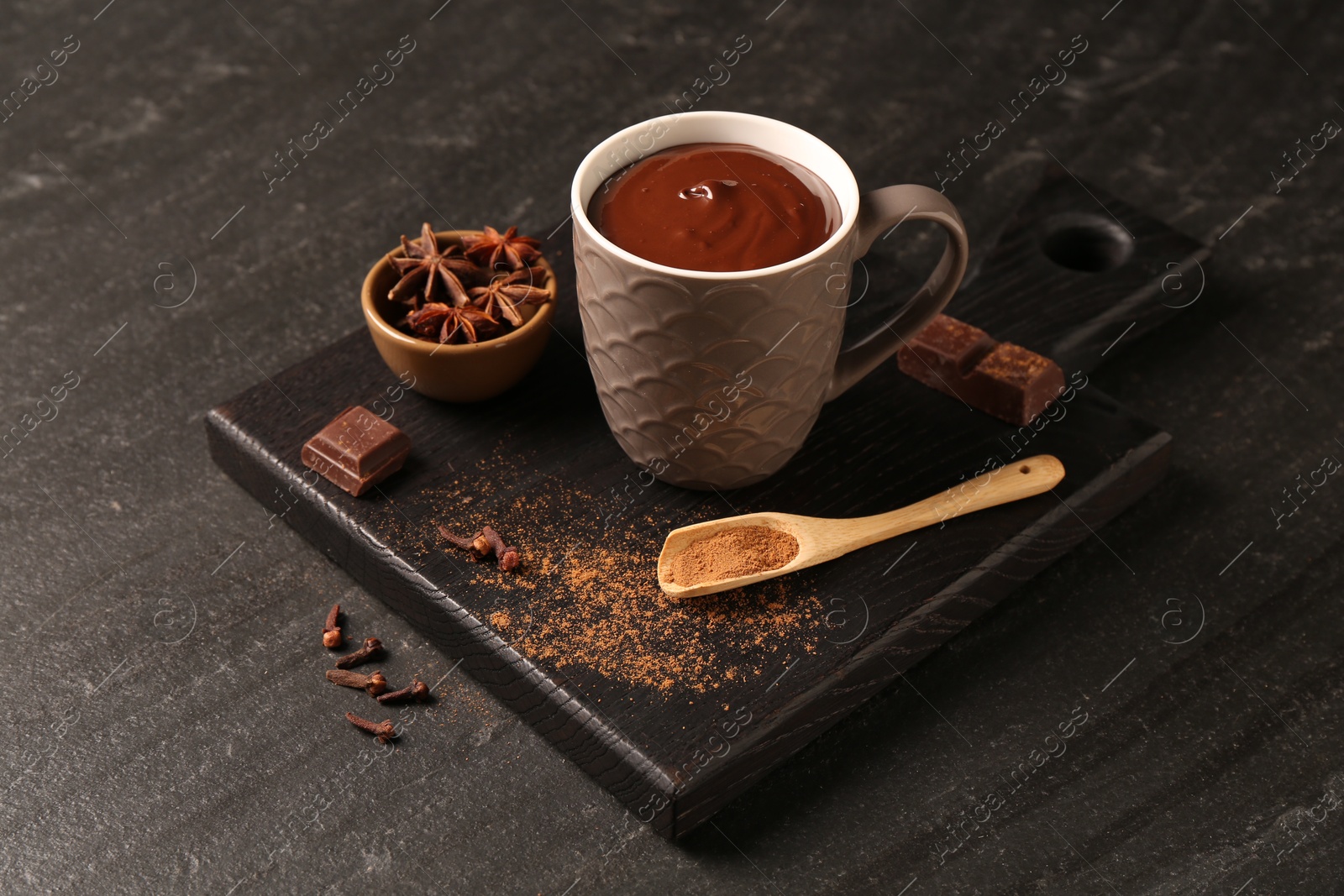 Photo of Tasty melted chocolate in cup and spices on dark textured table, closeup