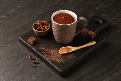 Photo of Tasty melted chocolate in cup and spices on dark textured table, closeup