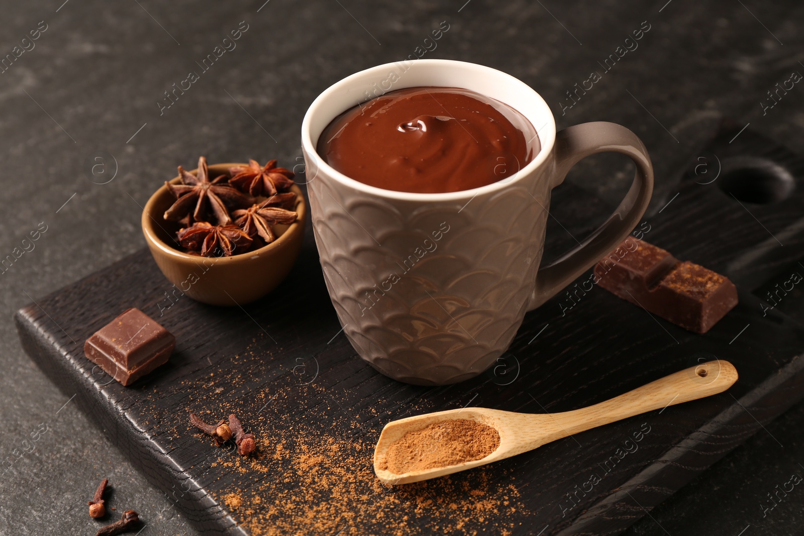 Photo of Tasty melted chocolate in cup and spices on dark textured table, closeup