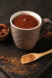 Tasty melted chocolate in cup and spices on dark table, closeup