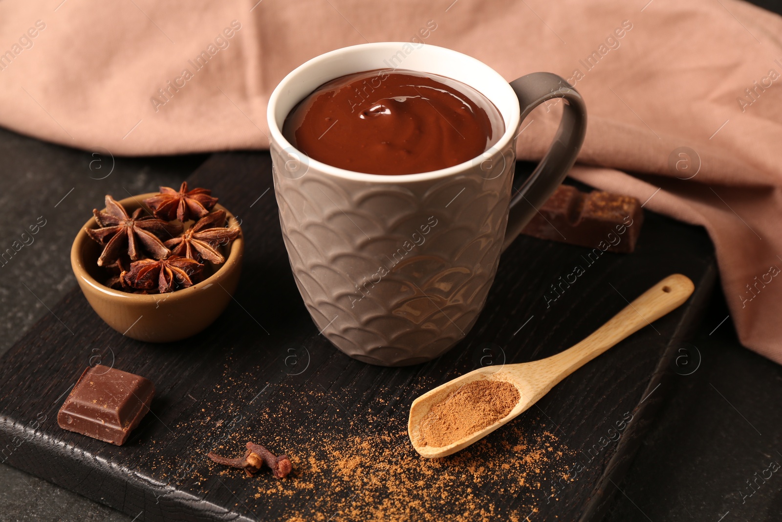 Photo of Tasty melted chocolate in cup and spices on dark textured table, closeup