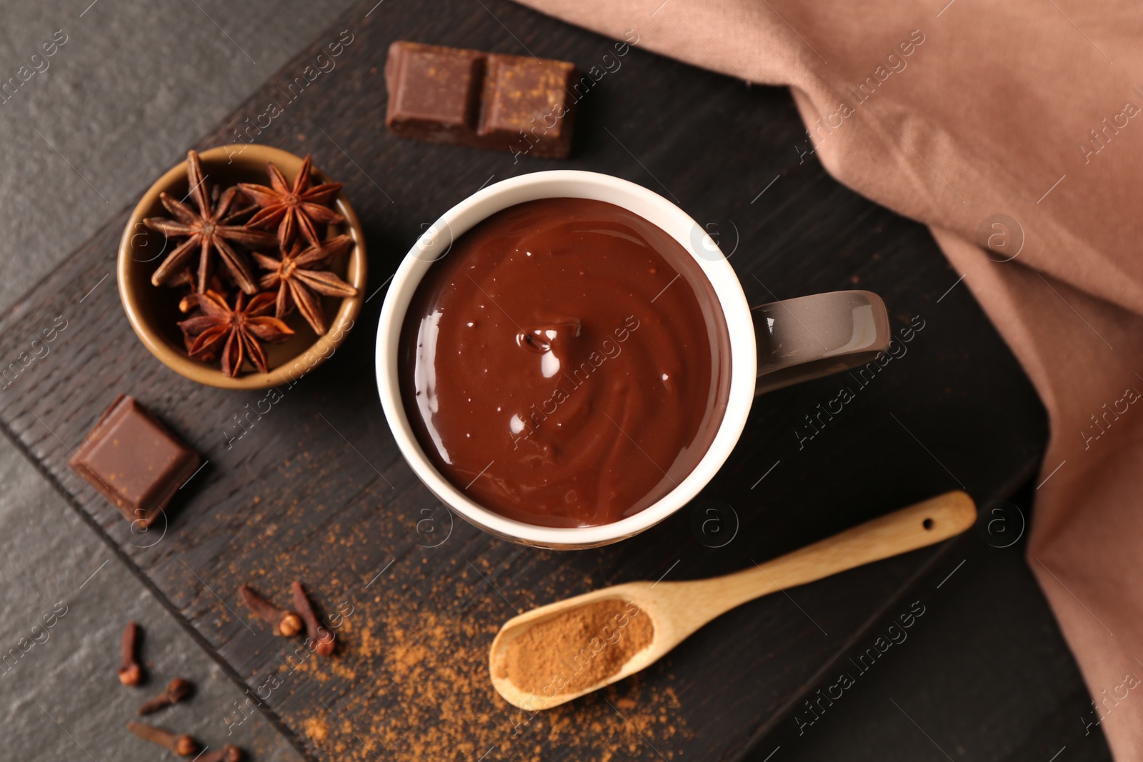 Photo of Tasty melted chocolate in cup and spices on dark textured table, top view