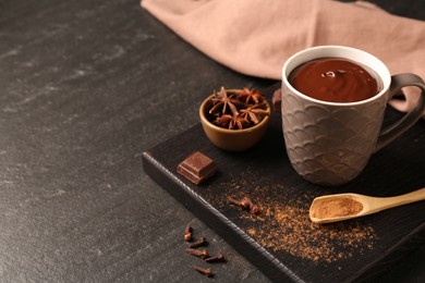 Photo of Tasty melted chocolate in cup and spices on dark textured table, closeup. Space for text