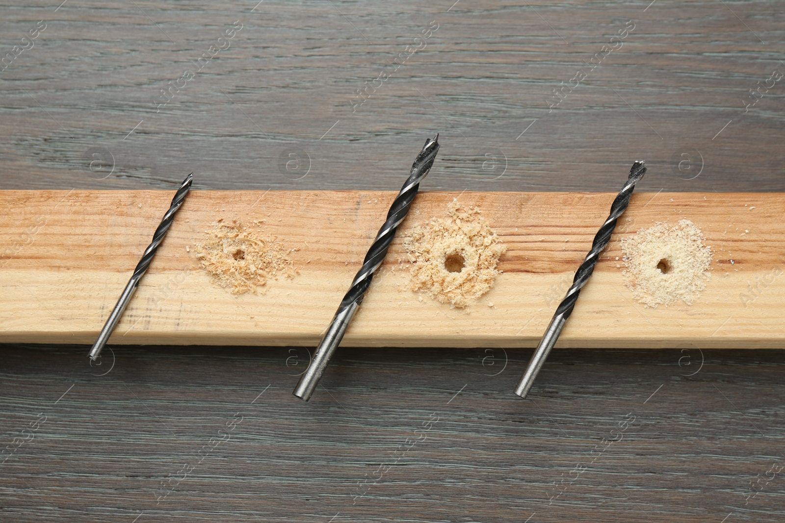 Photo of Plank with holes, drill bits and sawdust on wooden table, flat lay