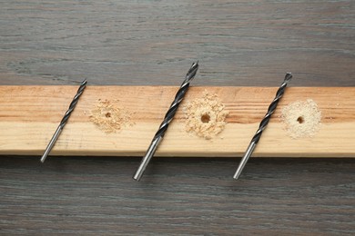 Plank with holes, drill bits and sawdust on wooden table, flat lay