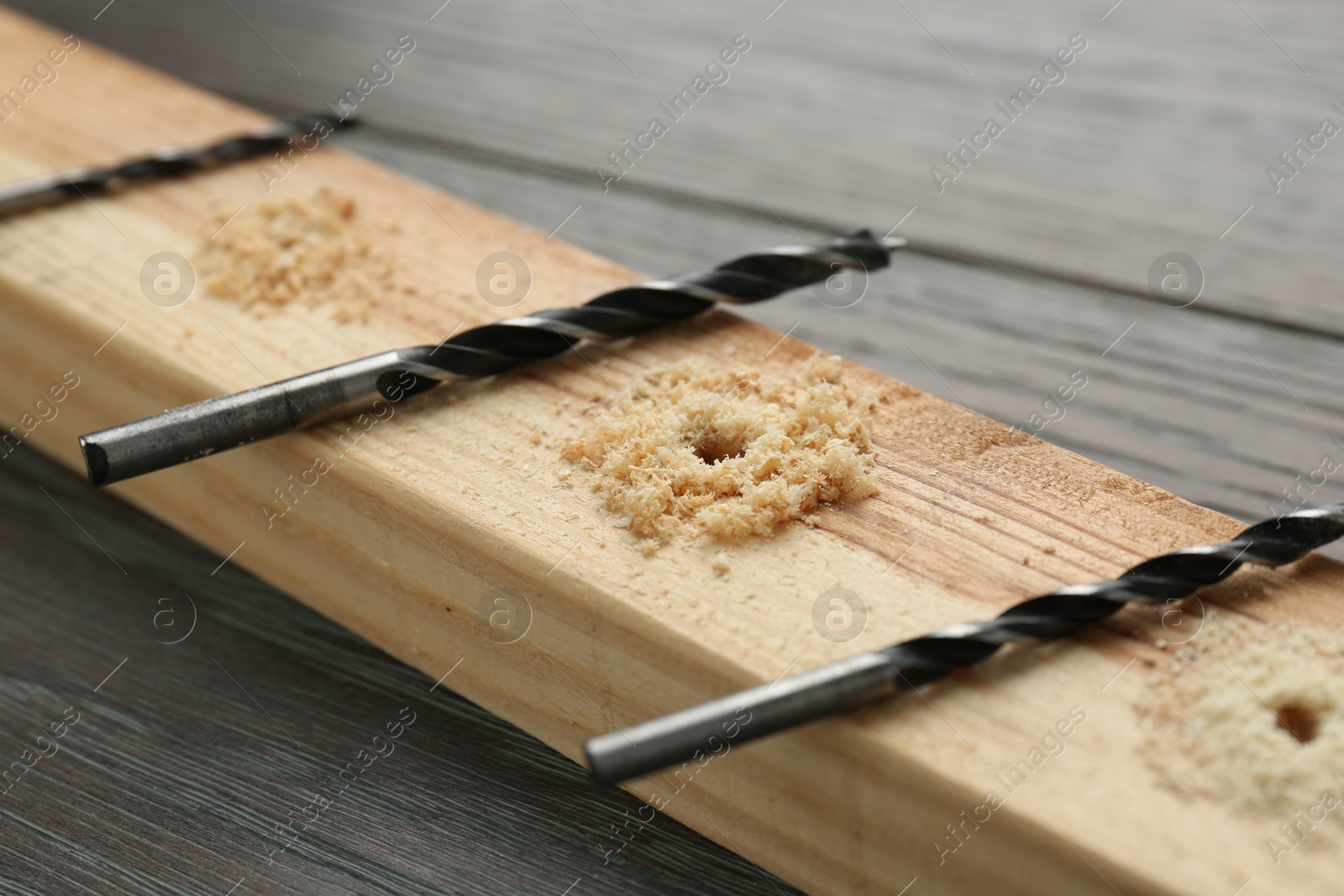 Photo of Plank with holes, drill bits and sawdust on wooden table, closeup