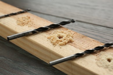 Photo of Plank with holes, drill bits and sawdust on wooden table, closeup