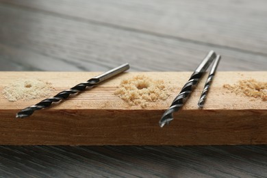 Photo of Plank with holes, drill bits and sawdust on wooden table, closeup