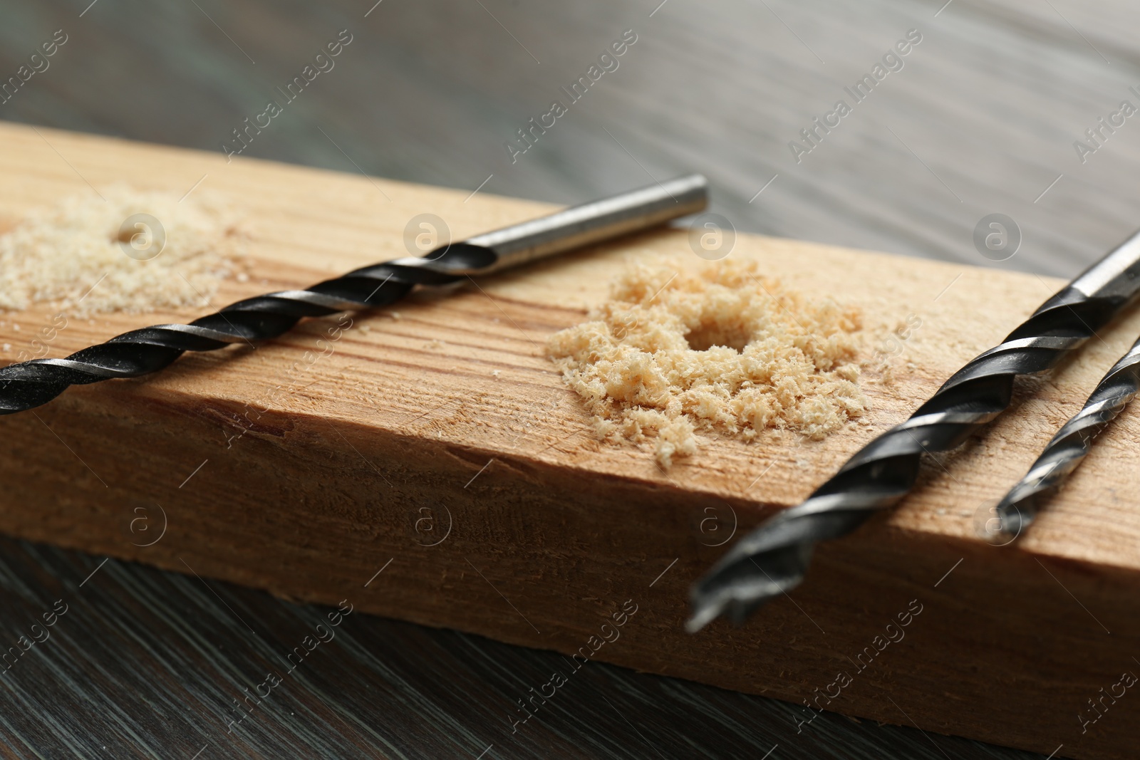 Photo of Plank with holes, drill bits and sawdust on wooden table, closeup