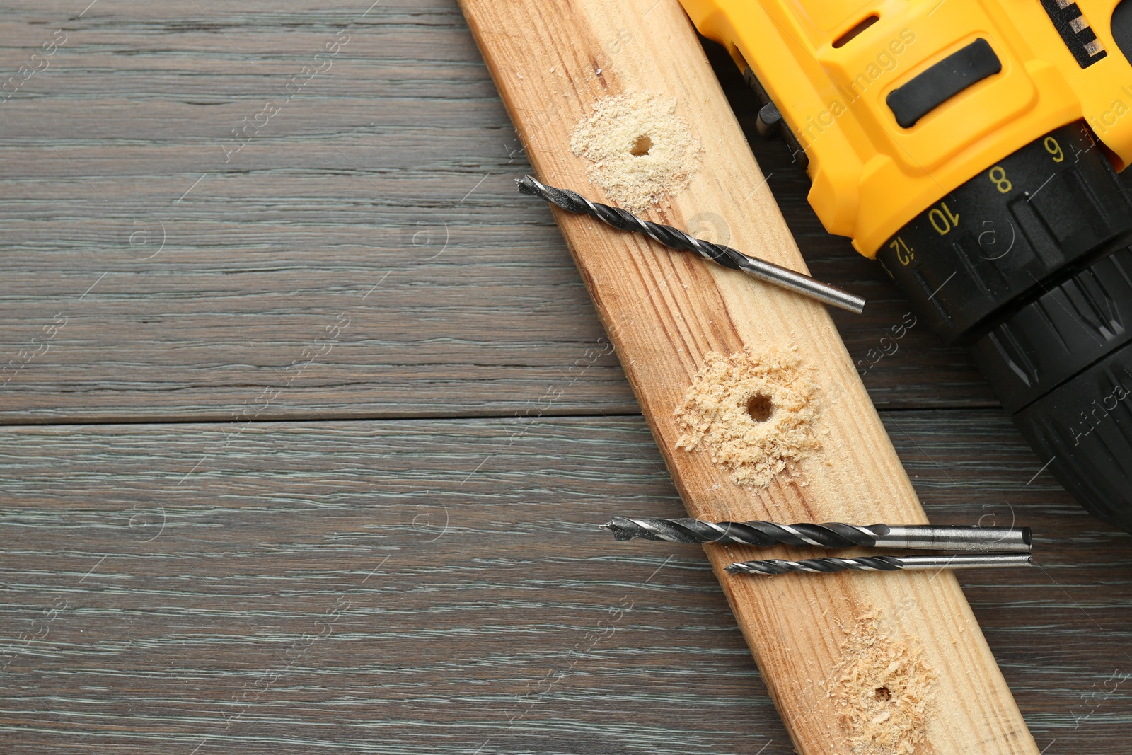 Photo of Cordless electric drill, bits and plank on wooden table, flat lay. Space for text