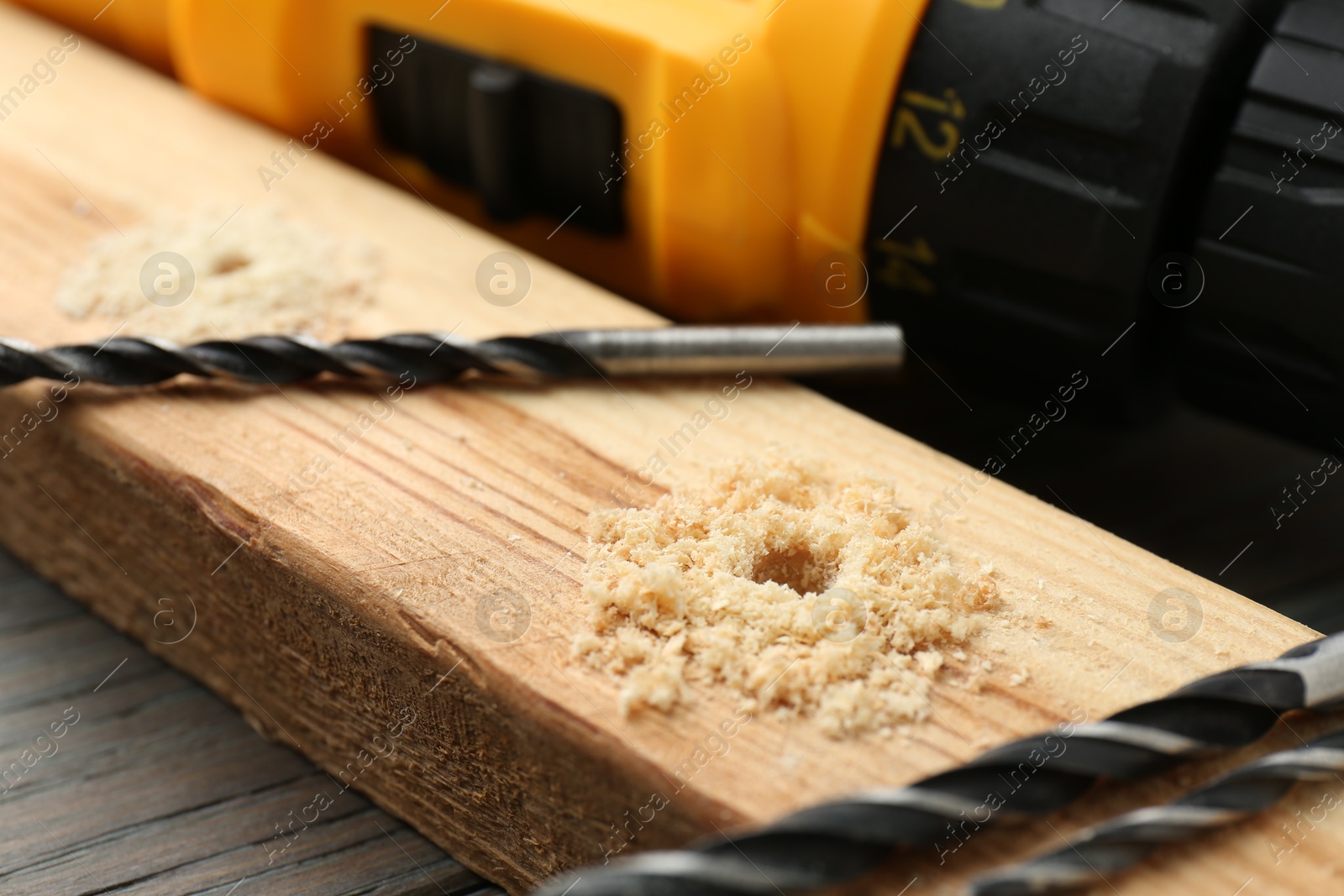 Photo of Bits, plank and cordless electric drill on wooden table, closeup