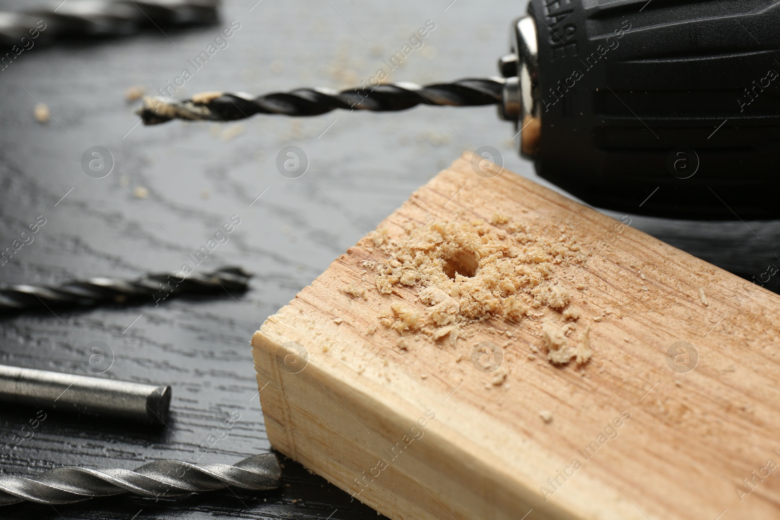 Photo of Cordless electric drill, bits and plank on black wooden table, closeup