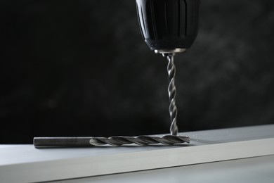 Drilling hole in plank on white table against black background, closeup