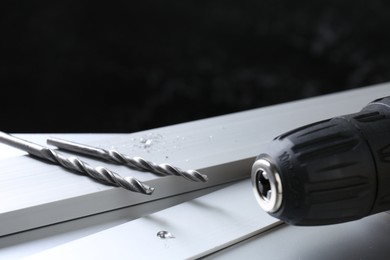 Photo of Bits, plank and cordless electric drill on white table against black background, closeup