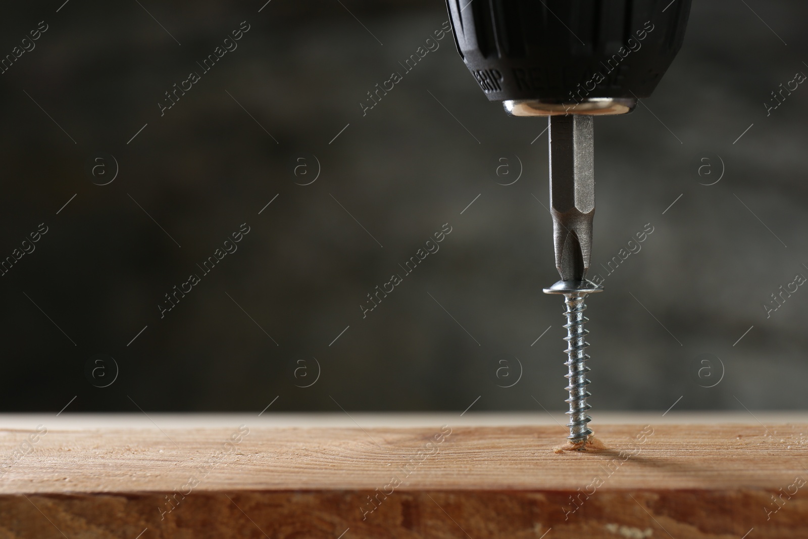 Photo of Screwing screw into wooden plank against gray background, closeup. Space for text