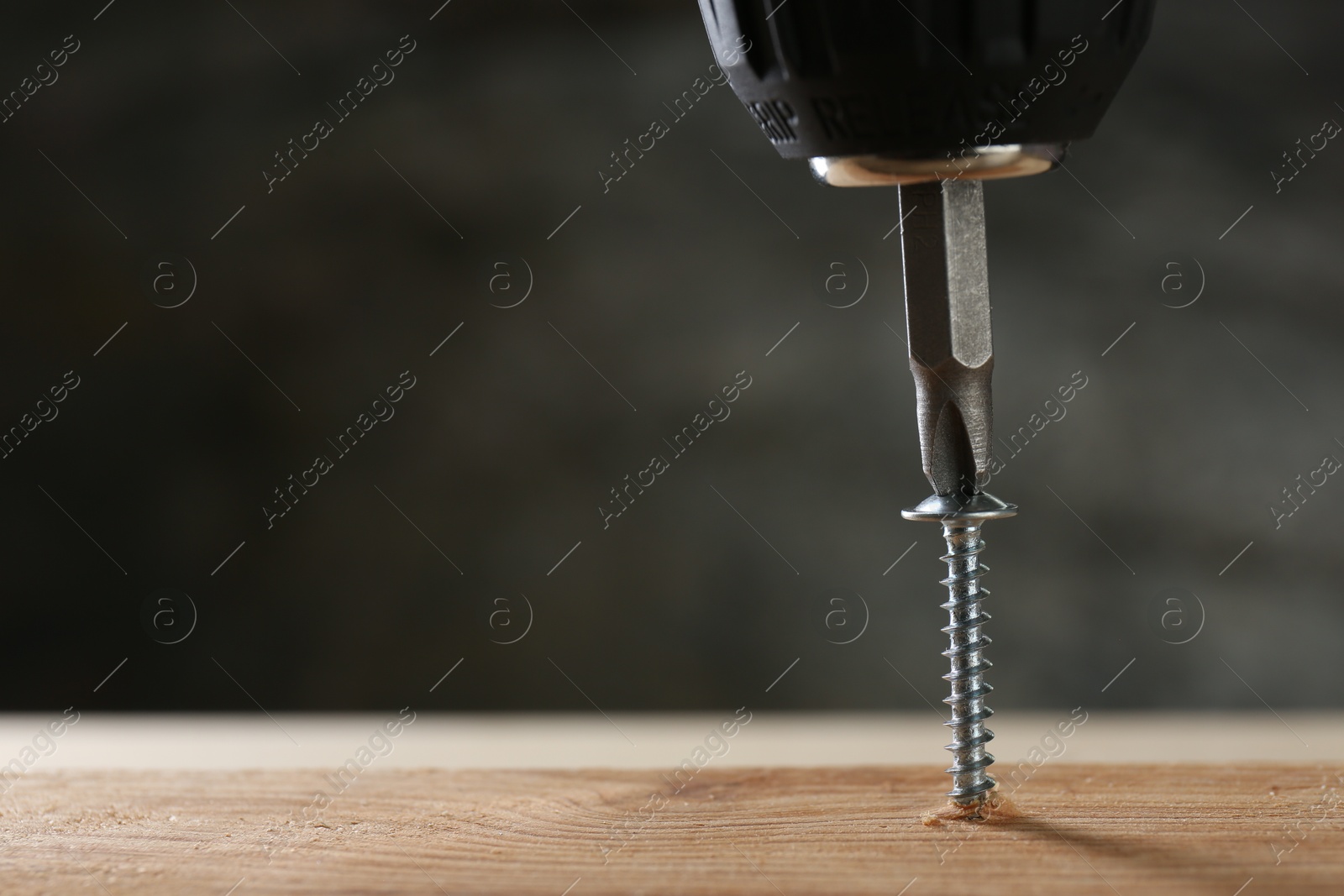 Photo of Screwing screw into wooden plank against gray background, closeup. Space for text