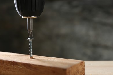 Photo of Screwing screw into wooden plank against gray background, closeup. Space for text