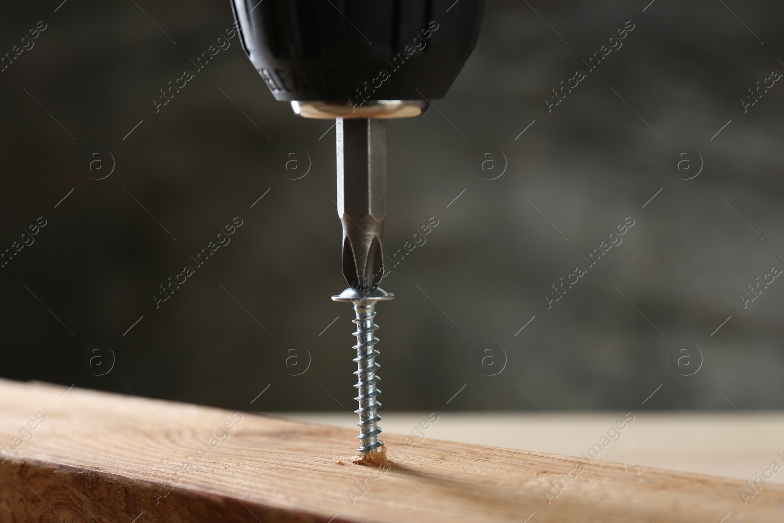 Photo of Screwing screw into wooden plank against gray background, closeup