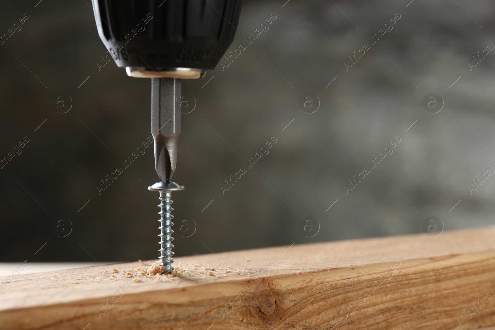 Photo of Screwing screw into wooden plank against gray background, closeup. Space for text