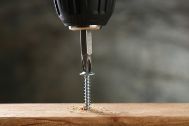 Photo of Screwing screw into wooden plank against gray background, closeup