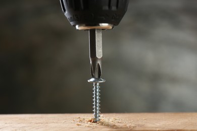 Photo of Screwing screw into wooden plank against gray background, closeup