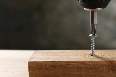 Photo of Screwing screw into wooden plank against gray background, closeup. Space for text