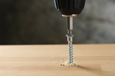 Photo of Screwing screw into wooden plank against gray background, closeup