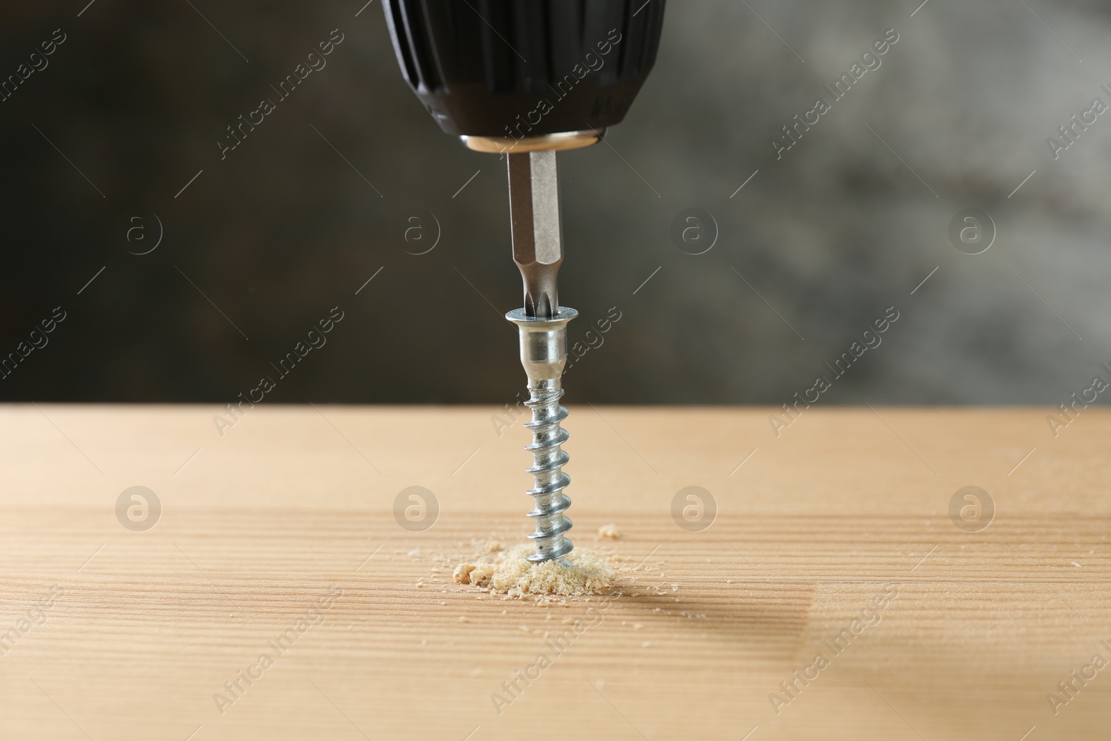 Photo of Screwing screw into wooden plank against gray background, closeup