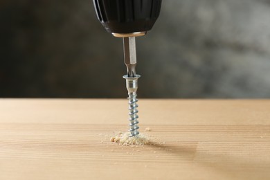 Photo of Screwing screw into wooden plank against gray background, closeup