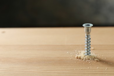 Photo of Screw in wooden plank and sawdust against gray background, space for text