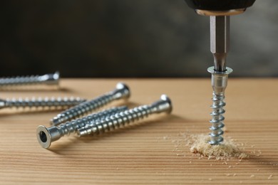 Screwing screw into wooden plank against gray background, closeup