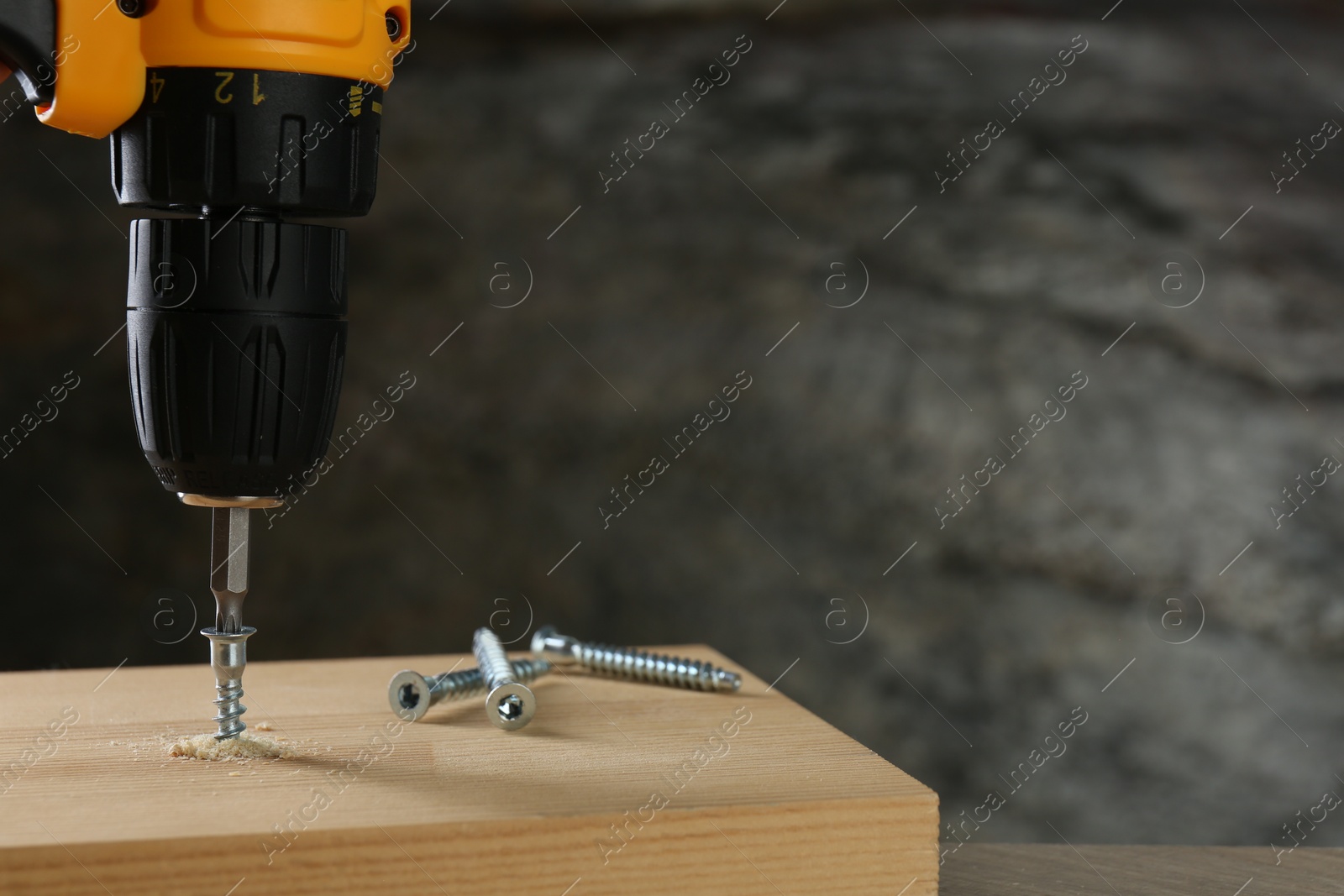 Photo of Screwing screw into wooden plank against gray background, closeup. Space for text