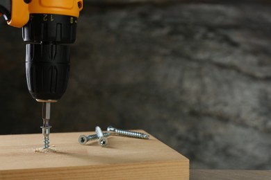 Photo of Screwing screw into wooden plank against gray background, closeup. Space for text