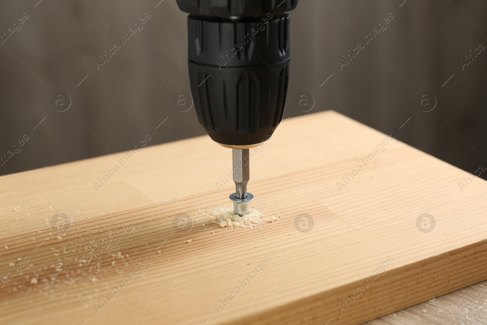 Photo of Screwing screw into wooden plank against gray background, closeup