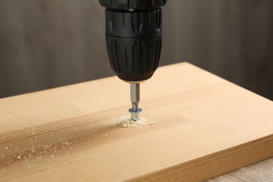 Screwing screw into wooden plank against gray background, closeup