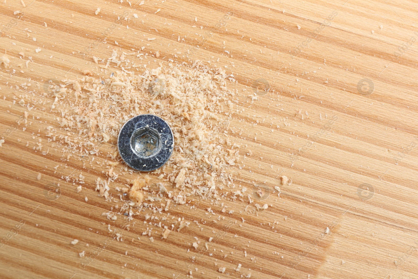 Photo of Screw in wooden plank and sawdust, top view