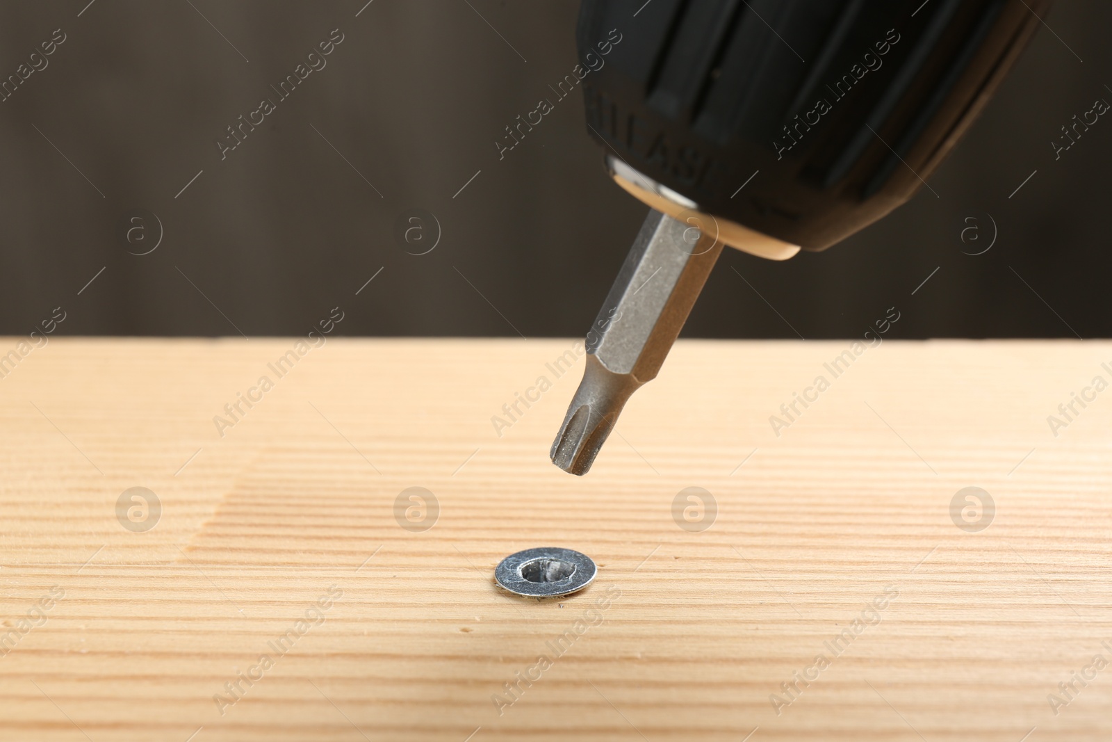 Photo of Screwing screw into wooden plank against gray background, closeup