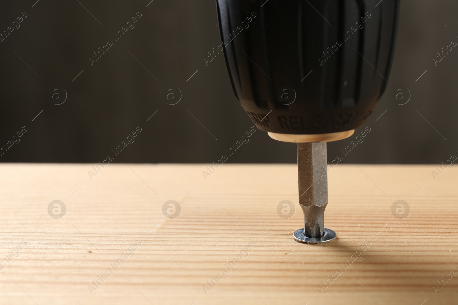 Photo of Screwing screw into wooden plank against gray background, closeup. Space for text